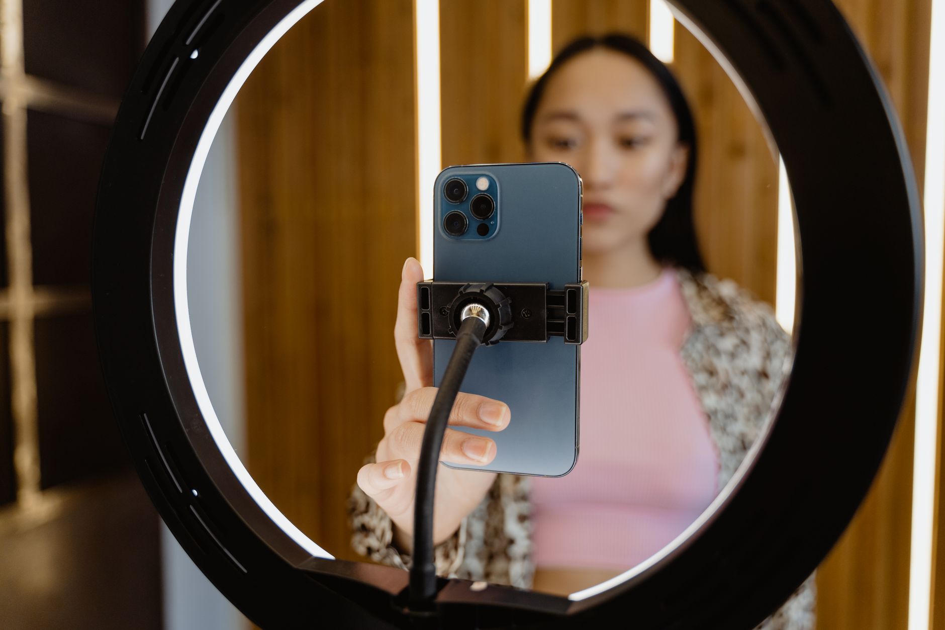 A woman framed by a ring light as she sets up a smartphone on a flexible stand to film
