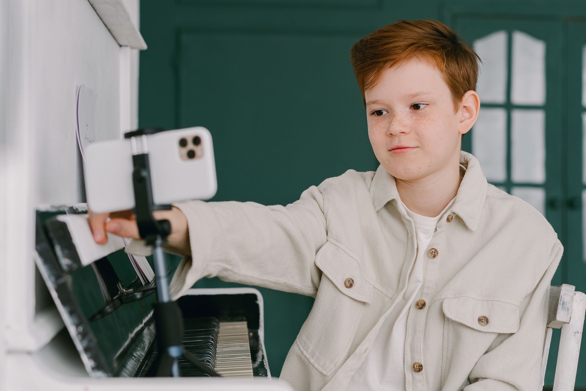 A young person at a piano reaching out to position a smartphone on a small tripod